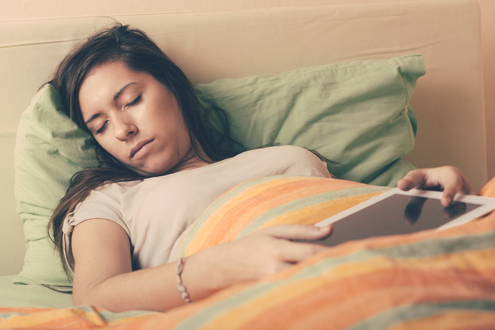 Young Woman Falling Asleep while Using Digital Tablet on Bed